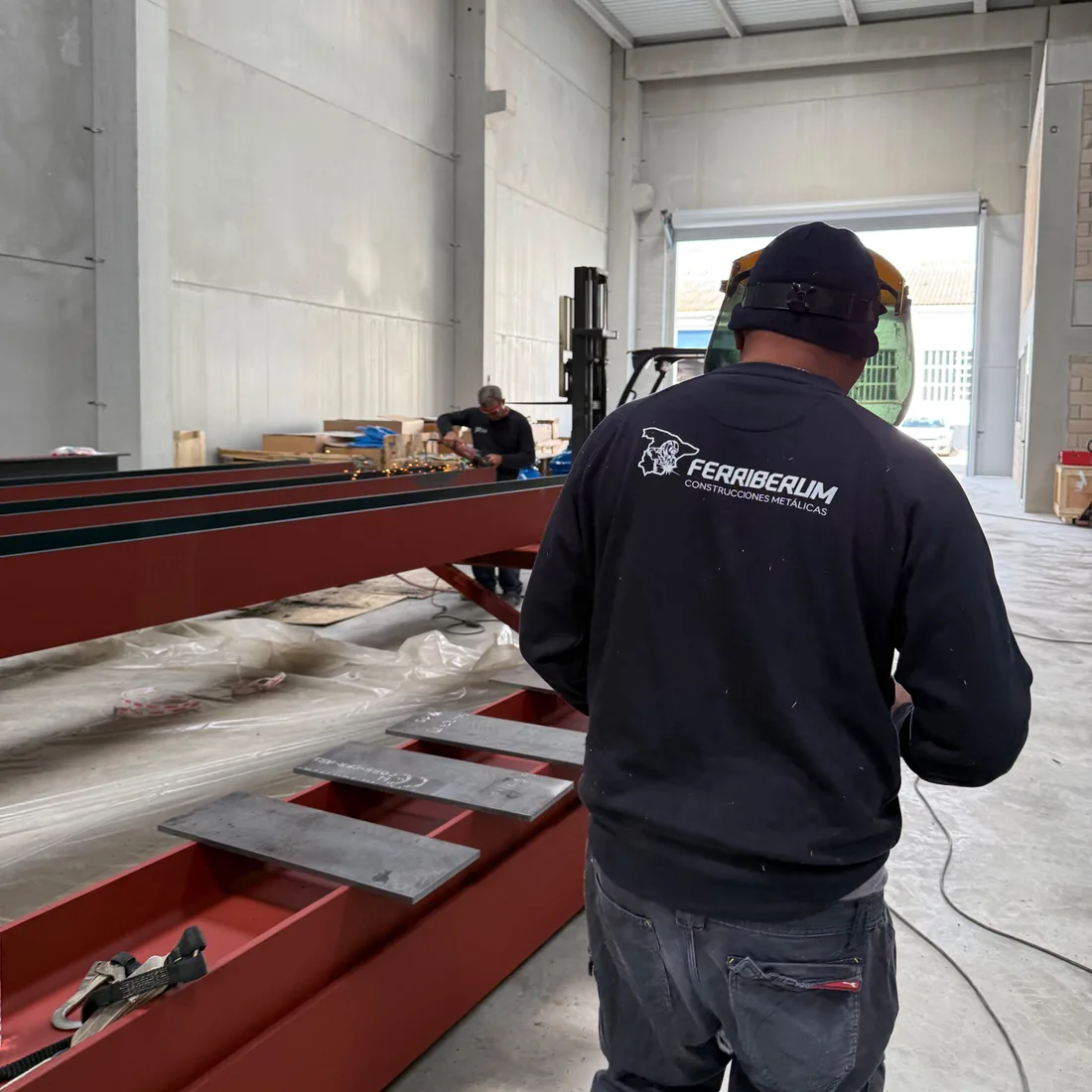 Operario de Ferriberum, de espaldas, trabajando en una nave con vigas de estructura metálica